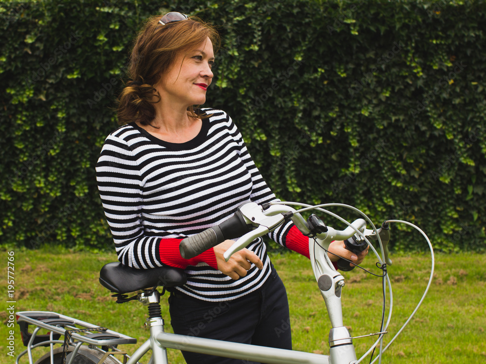 Obraz premium Portrait of a middle aged woman smiling leaning on a bicycle.