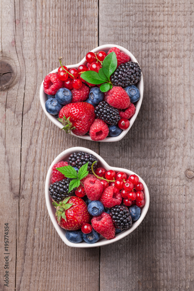 Berries fresh mix in heart shaped ceramic jars overhead on wooden table background in studio Berries fresh mix in heart shaped ceramic jars overhead on wooden table background in studio
