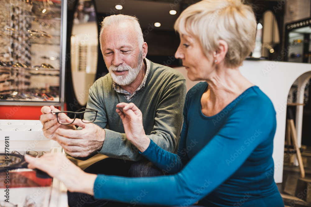 Happy senior couple choosing together eyeglasses frame in optical store. Happy senior couple choosing together eyeglasses frame in optical store.