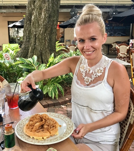 Beautiful blonde woman eating delicious Chicken & Waffle with maple syrup in New Orleans (Louisiana - USA)