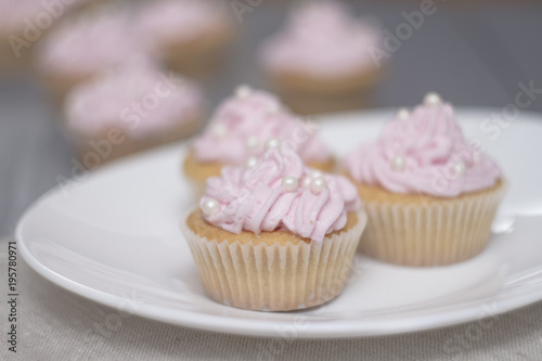 four cupcakes on grey wooden table, three cupcakes on oval white plate. Close up