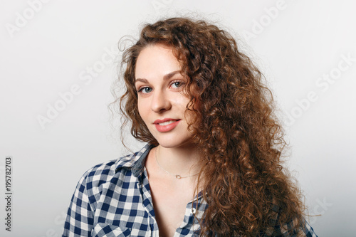 Horizontal portrait of delighted pleasant looking young female with curly hair, blue eyes and healthy skin, wears casual checkered shirt, isolaed over white background. Positive emotions concept