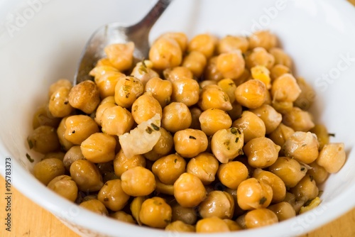 Pile of boiled chickpeas in white bowl with spoon.