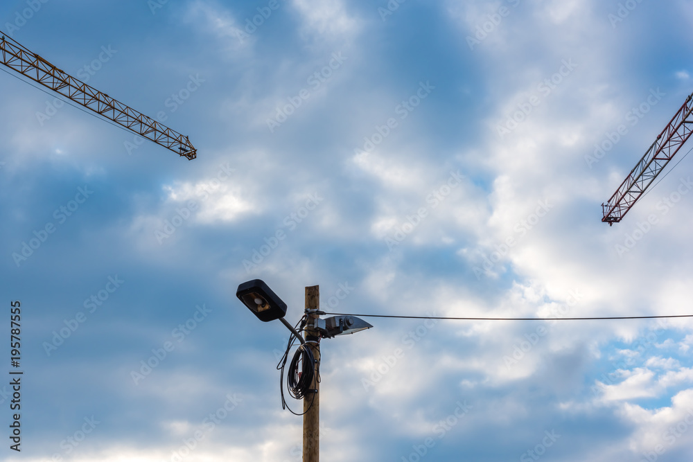 two construction cranes a street lighting and a cable two construction cranes a street lighting and a cable