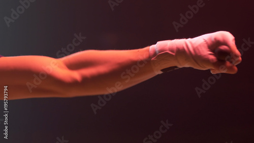 Close up shot of boxer's hands clenched into a fist on a dark red background. Fighter, boxer hand punching bag. Close-up.