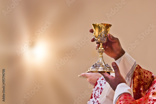 hands of the priest raise the blood of Christ