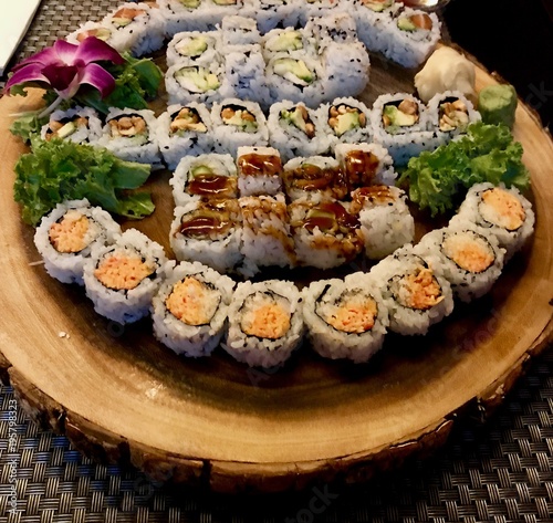 Delicious Sushi Plate with an assortment of different roles including salmon, shrimp, cucumber and avocado maki and sashimi decorated with a beautiful orchid flower