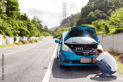 Fotografia Man sitting on the road with engine malfunction car in the middle of the road