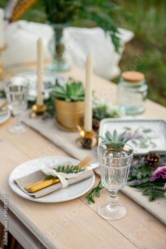Decorated elegant wooden table in rustic style with eucalyptus and flowers  porcelain plates  glasses  napkins and cutlery