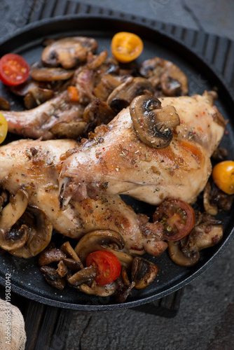 Close-up of roasted rabbit meat with champignons and cherry tomatoes, elevated view, vertical shot