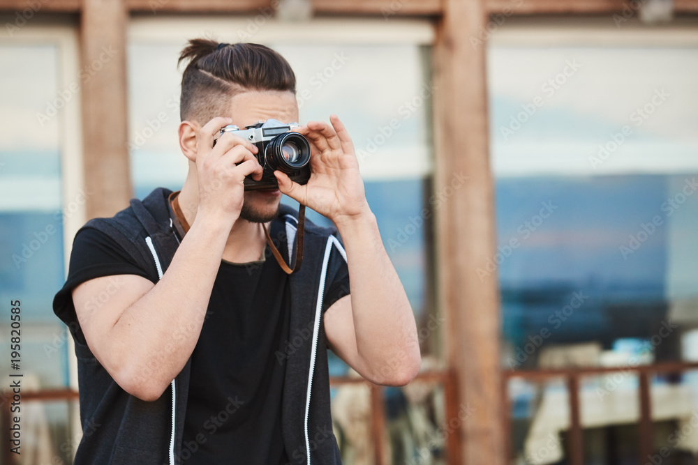 In search of best angle to create masterpiece. Portrait of dreamy good-looking caucasian guy in trendy outfit taking photos on street, looking through camera, focusing on model to make great shot In search of best angle to create masterpiece. Portrait of dreamy good-looking caucasian guy in trendy outfit taking photos on street, looking through camera, focusing on model to make great shot
