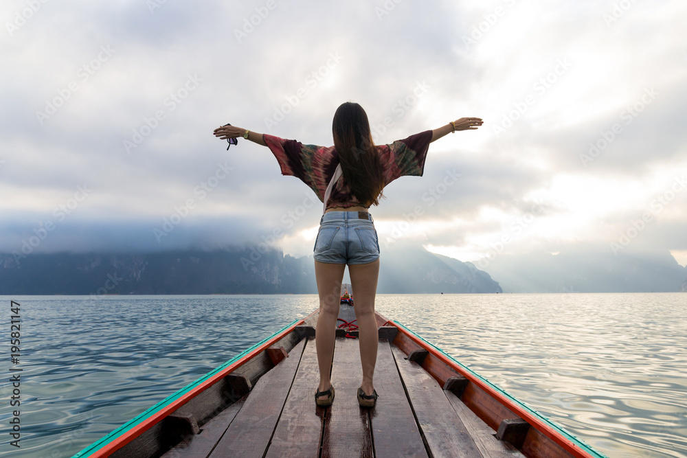 Back view of asian young woman traveling by wooden boat at sunrise