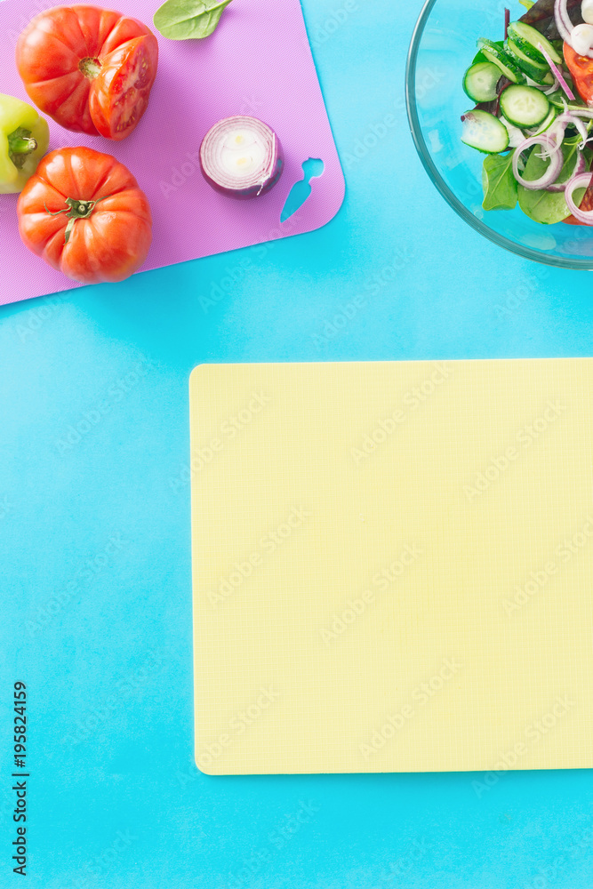 Empty kitchen cutting board with ingredients for cooking summer salad on blue background, top view. Healthy food concept. Diet food