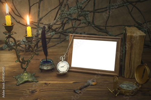 Empty photo frame with copy space and diary book of adventurer on wooden table with compass and rusty key in the light of burning candle. Vintage background. Traveller concept. Explorer.