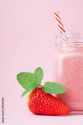Fresh strawberry smoothie or milkshake in mason jar decorated mint on pink pastel background. Healthy food for breakfast and snack.