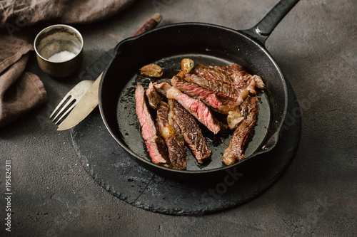 Slices juicy beef steak on vintage cast-iron frying pan