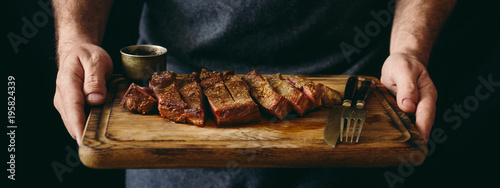 Man holding juicy grilled beef steak with spices on cutting board