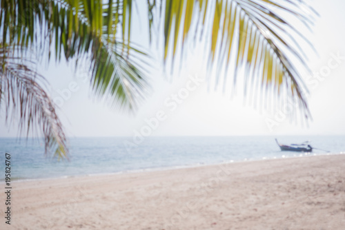 Blurred tropical palm leaves over sandy beach sea with fishing boat and sky  summer background.