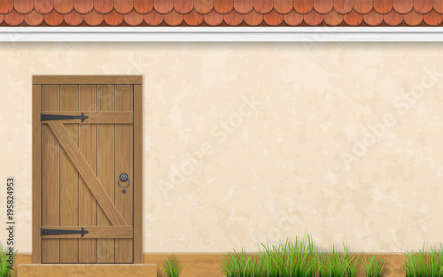Stucco wall of a house with an old wooden door. Fence and grass in a front garden.