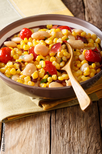 Home succotash of beans, tomatoes, peppers and bacon close up in a bowl. vertical