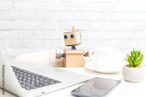 The robot is sitting at the table and next to the laptops with the phone. Artificial Intelligence