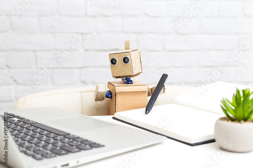The robot sits at the desk and looks at the computer monitor. Artificial Intelligence.