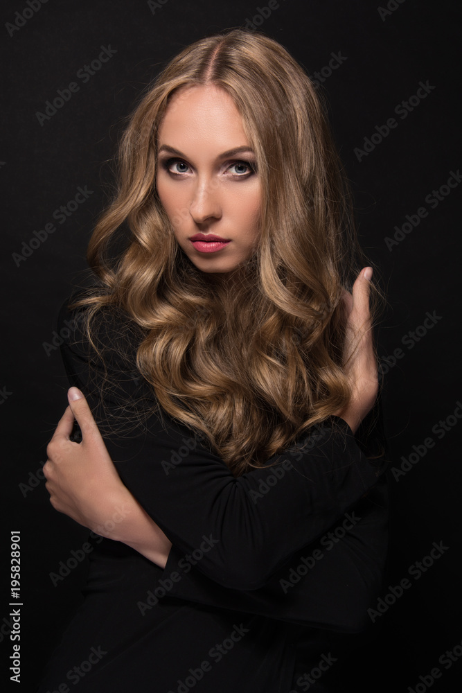 Fototapeta premium Portrait of a beautiful young sexy girl with long blond hair and evening make-up on a black background.
