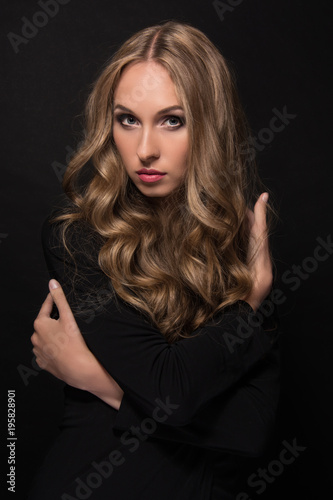 Portrait of a beautiful young sexy girl with long blond hair and evening make-up on a black background.