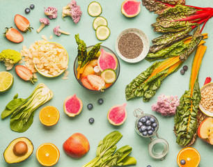 Healthy food ingredients flat lay with various fruits , vegetables, seeds and nut on light mint background. Mixer for detox drinks making, top view. Dieting and clean eating concept