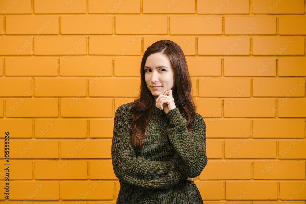 Beautiful red-haired girl wearing glasses and a green sweater is smiling against a yellow brick wall background. Beautiful red-haired girl wearing glasses and a green sweater is smiling against a yellow brick wall background.