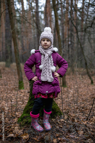 Little girl posing near the old stump in autumn forest.