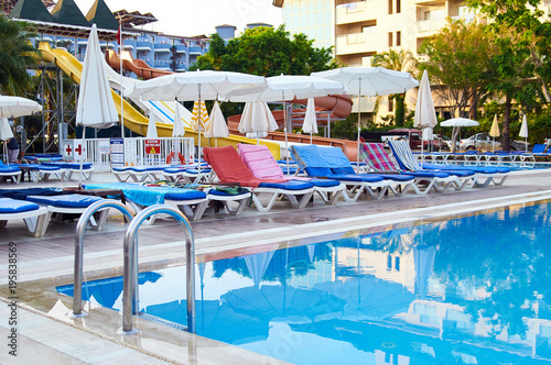 Swimming pool, sun loungers with towels, beach umbrellas, but no people. A typical summer vacation is all inclusive. A hot summer day. Water slides, mini water park in the background.