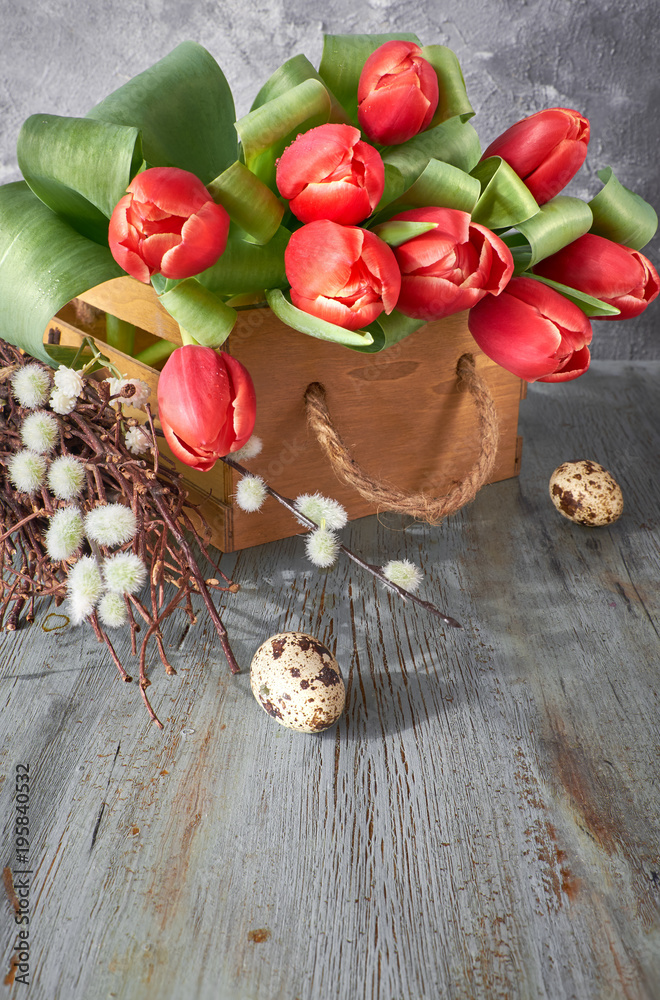 Fototapeta premium Spring celebration background: bunch of red tulips, spring decorations and painted eggs on gray rustic wood