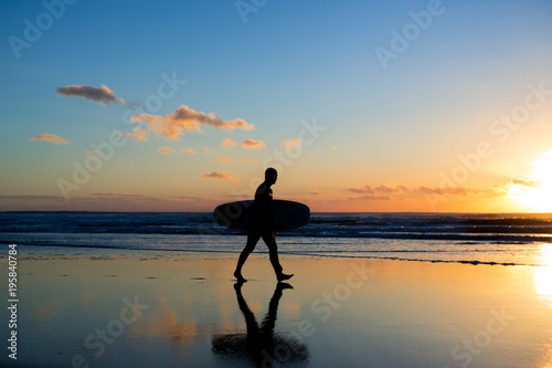 Sunset surfing. Silhouette of man surfer walking with a surf board in his hands across the ocean shore. © sergiophoto