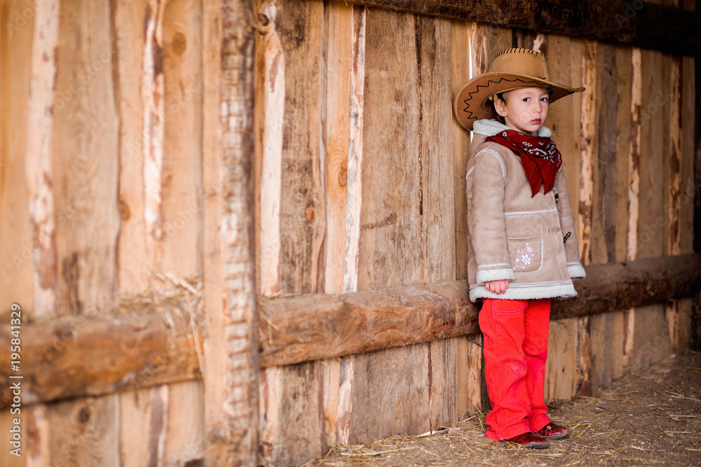 a little girl in a cowboy hat stands near the wall of a barn
