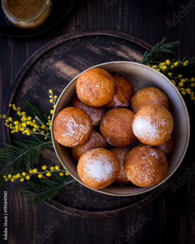 On a plate donuts with sugar powder, decorated with mimosa flowers. Wooden background