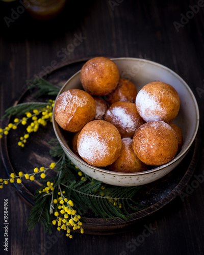On a plate donuts with sugar powder, decorated with mimosa flowers. Wooden background