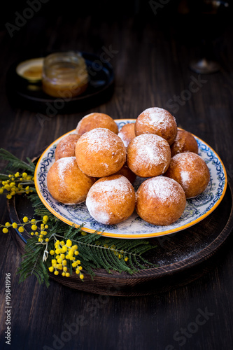 On a plate donuts with sugar powder, decorated with mimosa flowers. Wooden background