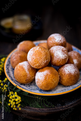 On a plate donuts with sugar powder, decorated with mimosa flowers. Wooden background