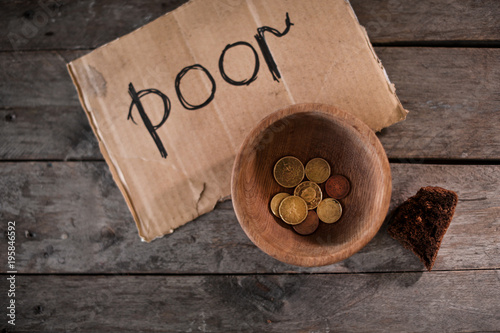 Coins and piece of cardboard with word POOR on wooden background
