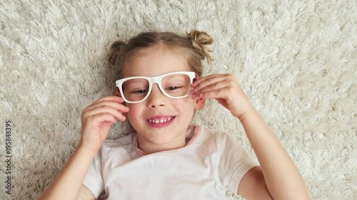 Happy smiling girl putting on optical glasses lying on the floor. Concept of vision and health care.