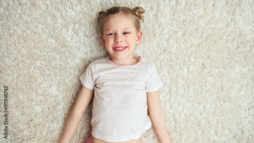 Adorable playful girl imagining fly, lying on carpet indoors. Cute little girl having fun at home. 