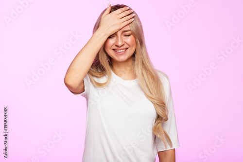 Foto Cheerful young female making facepalm, holding hand on forehead, did something stupid and smiling