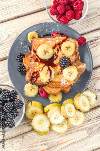 vertical shot of a tower of french toast with fried plantain and berries in natural wood