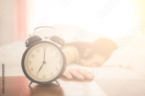 Alarm clock with a woman sleeping in the background on bed