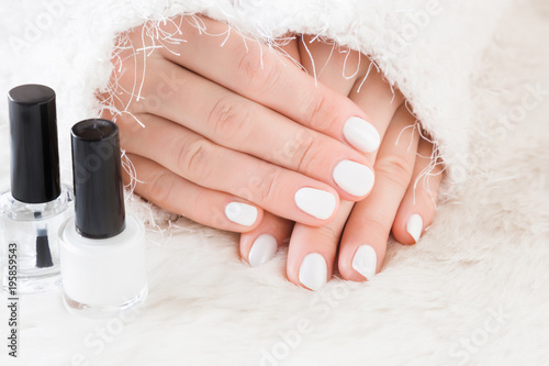 Beautiful groomed woman s hands with nail varnish bottle on the fluffy mat. Nail varnishing in white color. Manicure  pedicure beauty salon concept.