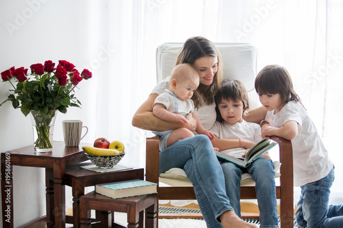Mother  playing with her toddler boy and his older brother  reading book  smiling