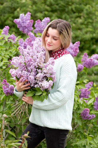 Beautiful young girl with a bouquet of lilacs in the garden