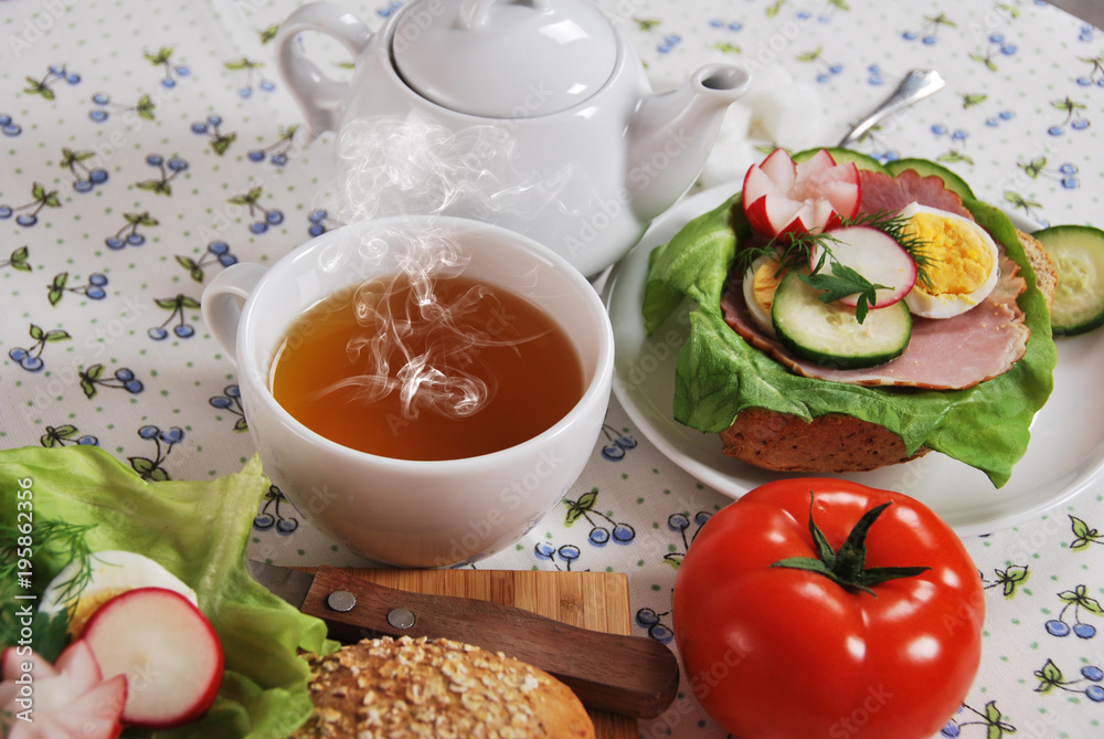 hot tea in a cup for breakfast with healthy sandwiches with lettuce, cucumber, egg, ham and radish flower with fresh dill hot tea in a cup for breakfast with healthy sandwiches with lettuce, cucumber, egg, ham and radish flower with fresh dill