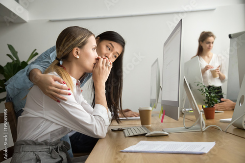Asian colleague embracing supporting caucasian woman reading bad news in email, teammate comforting stressed frustrated female coworker upset by dismissal, helping to solve problem online in office photo